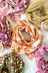 Petit foulard "Manika Flora Bold Orange" de la marque Apaches Collection. Accessoire tendance en tissu léger avec un motif floral vintage dans des tons chauds d'orange et beige. Idéal pour apporter une touche bohème et élégante à votre tenue. Peut être porté autour du cou, dans les cheveux ou en accessoire de sac.
