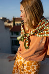 Grand foulard "Latika Pop Corn Olive" de la marque Apaches Collections. Accessoire en coton doux avec un motif original de fleurs et de rayures dans des tons vert olive, orange et beige. Idéal pour ajouter une touche bohème et colorée à votre tenue, il se porte autour du cou, en bandeau dans les cheveux ou en accessoire de sac.