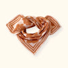 Petit foulard "Manika Flora Bold Orange" de la marque Apaches Collection. Accessoire tendance en tissu léger avec un motif floral vintage dans des tons chauds d'orange et beige. Idéal pour apporter une touche bohème et élégante à votre tenue. Peut être porté autour du cou, dans les cheveux ou en accessoire de sac.
