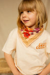 Grand foulard "Latika Joy Macadamia" de la marque Apaches Collections. Accessoire en coton doux avec un imprimé floral aux teintes vives de rouge, violet et orange, sublimé par des bordures beige rayées. Ce foulard polyvalent et tendance peut se porter en bandana, autour du cou ou comme accessoire de cheveux pour un style bohème et élégant.