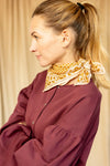 Petit foulard "Manika Mosaic Tobacco" de la marque Apaches Collections. Accessoire en coton doux avec un motif mosaïque géométrique et des bordures florales dans des tons tabac et beige. Idéal pour sublimer une tenue avec une touche bohème et chic, ce foulard peut se porter autour du cou, en bandeau ou en accessoire de sac.