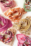 Petit foulard "Manika Mosaic Tobacco" de la marque Apaches Collections. Accessoire en coton doux avec un motif mosaïque géométrique et des bordures florales dans des tons tabac et beige. Idéal pour sublimer une tenue avec une touche bohème et chic, ce foulard peut se porter autour du cou, en bandeau ou en accessoire de sac.