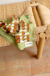 Grand foulard "Latika Pop Corn Olive" de la marque Apaches Collections. Accessoire en coton doux avec un motif original de fleurs et de rayures dans des tons vert olive, orange et beige. Idéal pour ajouter une touche bohème et colorée à votre tenue, il se porte autour du cou, en bandeau dans les cheveux ou en accessoire de sac.